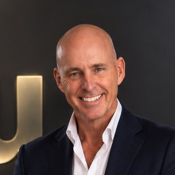 Nick Jeffries, founder of NU Projects, smiling, in a navy suit beside the gold #nu sign